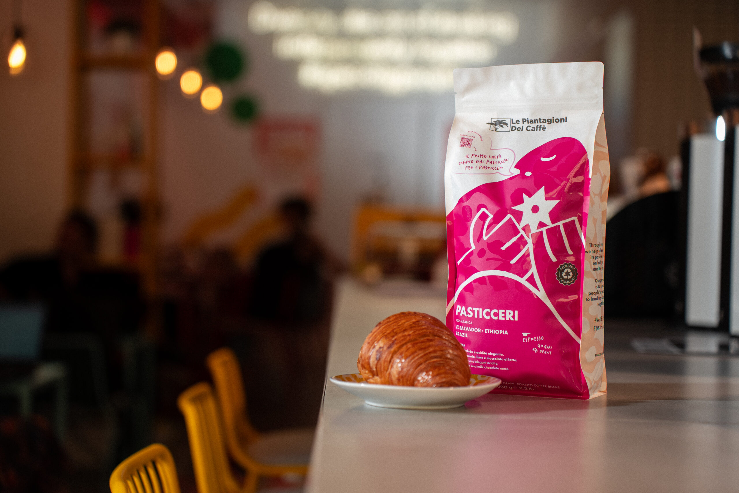 pacco di caffè speciality brand PASTICCERI su un bancone di una caffetteria con una brioche accanto